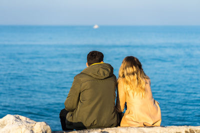 Rear view of couple sitting by sea against sky