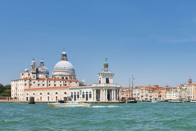 Buildings in sea against clear blue sky