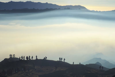 Silhouette people standing on mountain peak during foggy weather