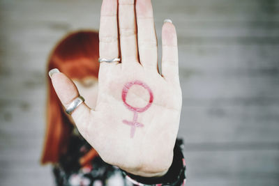Mid adult woman showing gender equality sign while standing against wall
