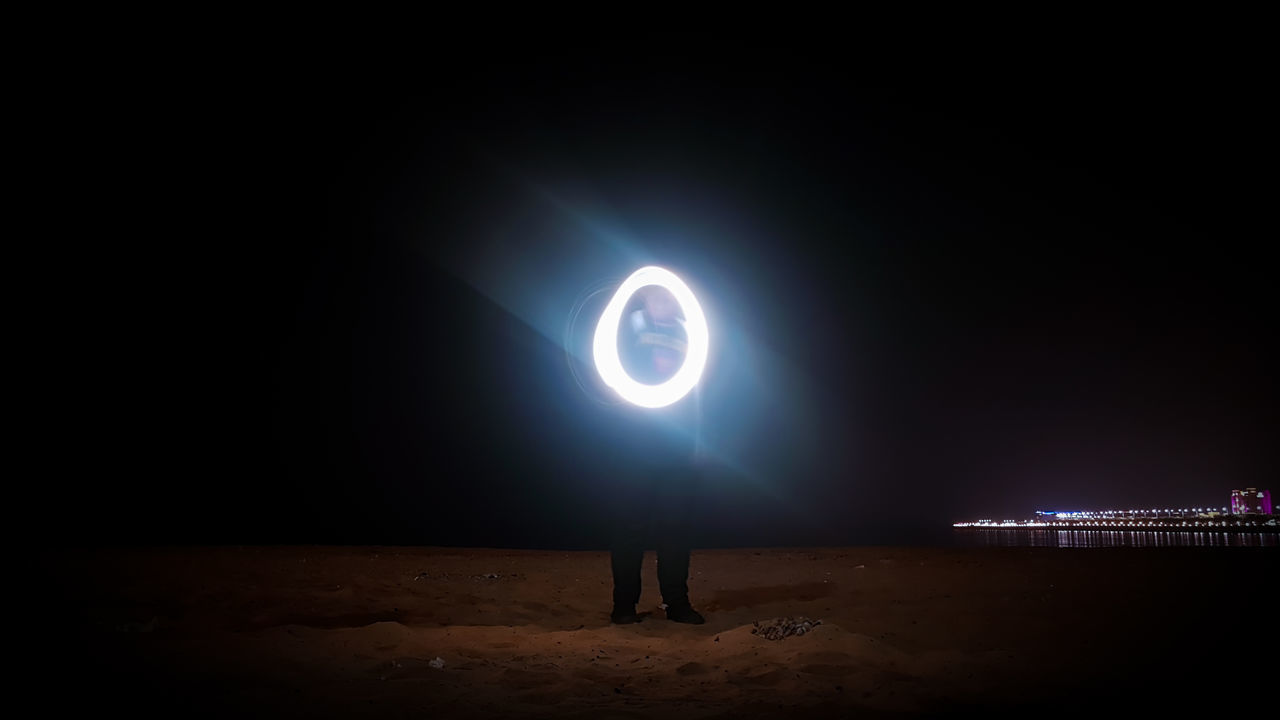 MAN STANDING ON ILLUMINATED LAND AT NIGHT