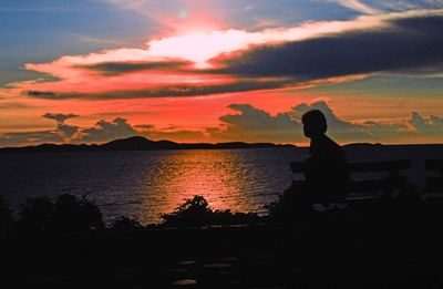 Silhouette man sitting by sea against sky during sunset