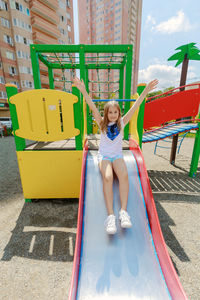 Full length of girl sitting on slide in playground