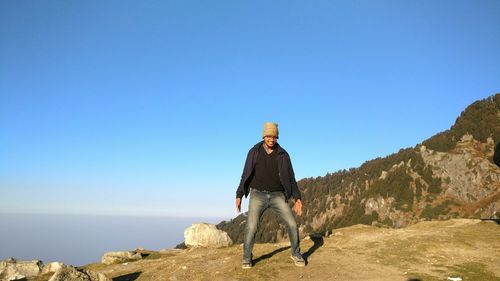 Portrait of young man standing on mountain against clear sky