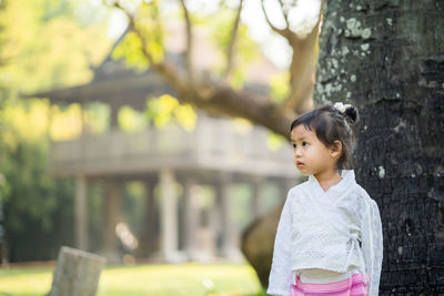 Girl standing on grass by tree trunk against building