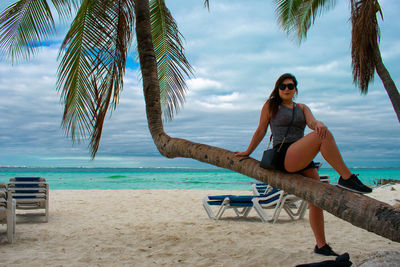 Portrait of woman sitting on palm tree at beach