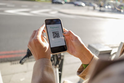 Woman making contactless payment using smart phone for renting bicycle