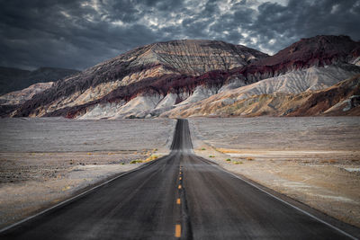 Road leading towards mountains against sky