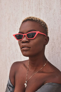 Close-up of young woman wearing sunglasses standing against wall