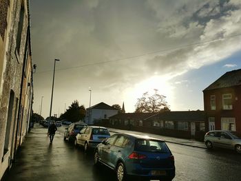 Cars parked on road in front of buildings against cloudy sky