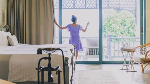 Rear view of woman standing on bed at home