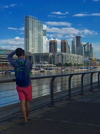 Rear view of man standing by railing against urban skyline