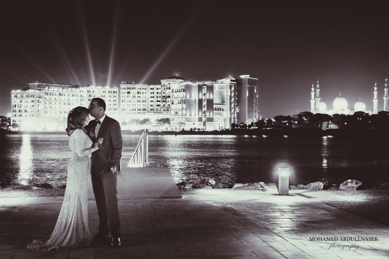 FULL LENGTH OF COUPLE STANDING AT ILLUMINATED CITY