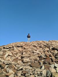Low angle view of man standing on rock against clear blue sky