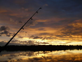 Silhouette fishing road by lake against cloudy sky during sunset