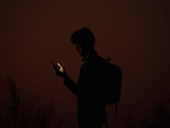 Side view of young man using phone against sky at night