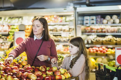 Mother and daughter choosing fresh apples at market stall