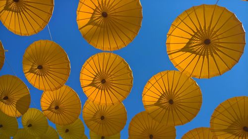 Low angle view of yellow umbrellas hanging against clear blue sky