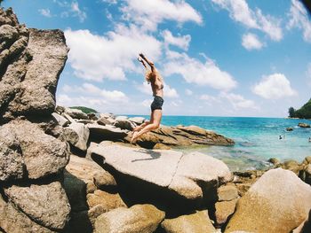 Young woman on rock by sea against sky