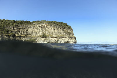 Rough cliff with green plants located near rippling clean sea