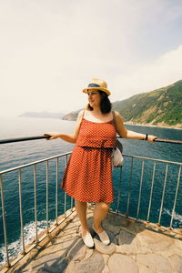 Woman standing by railing against sea against sky