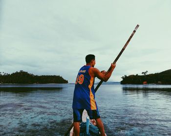 Rear view of man fishing in river against sky