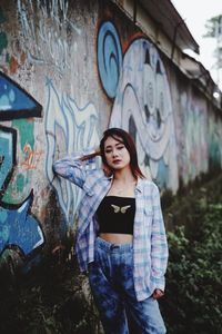 Portrait of young woman standing against graffiti wall