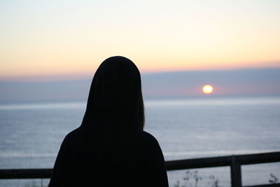 Rear view of woman standing against sea during sunset