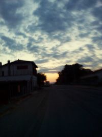 Road amidst houses against sky at sunset