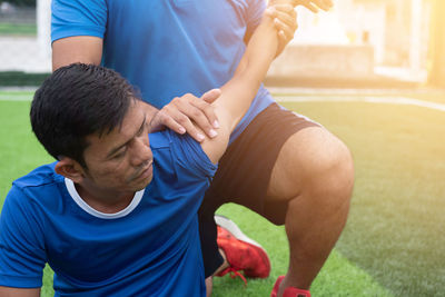 Low section of male physical therapist stretching soccer player hand on field