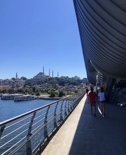 People on bridge in city against clear sky