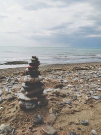 Man sitting on pebbles at beach against sky