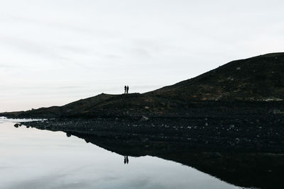 Silhouette person standing on shore against sky