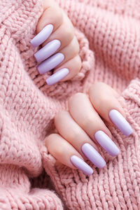 Girl's hands with a soft purple manicure. knitted pink sweater background. 