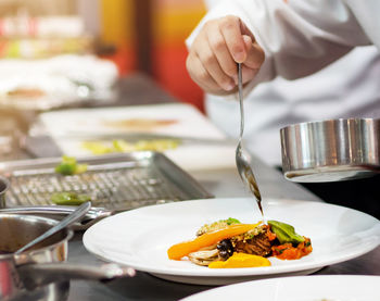 Midsection of person preparing food in plate on table