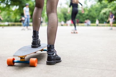 Low section of woman with skateboard standing on footpath in park