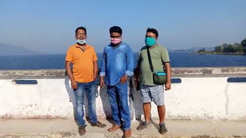 Portrait of friends standing by sea against blue sky