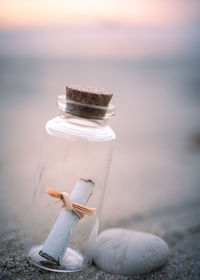 Close-up of a small glass bottle containing a paper message on the beach during sunrise