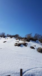 Snow covered landscape against clear blue sky