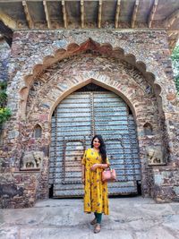Portraits- young women in colorful indianwear standing in front of rustic arched gate of a fort.