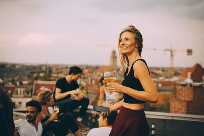 Smiling woman enjoying drink while partying with friends at rooftop