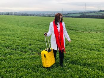 Woman holding luggage while standing on field