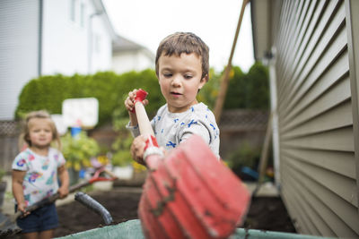 Young boy using red shovel in his backyard.