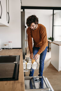 Man taking out cups from dishwasher in kitchen at home