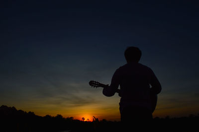 A man with a guitar strumming and looking at the sunset in the evening