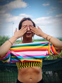 Young woman with hands covering eyes against sky