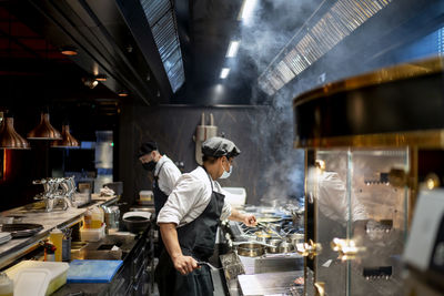 Chefs wearing protective face mask preparing dish in restaurant kitchen