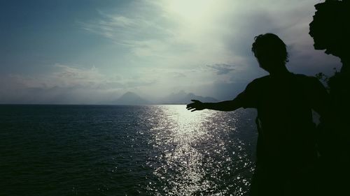 Silhouette man standing by sea against sky