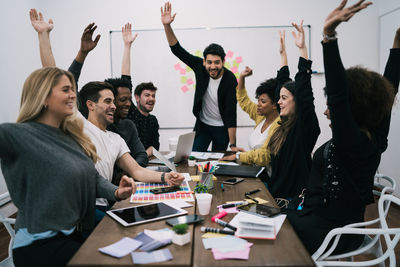 Happy colleagues with hand raised sitting on chairs in board room