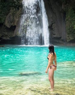 Seductive woman standing against waterfall at mountain